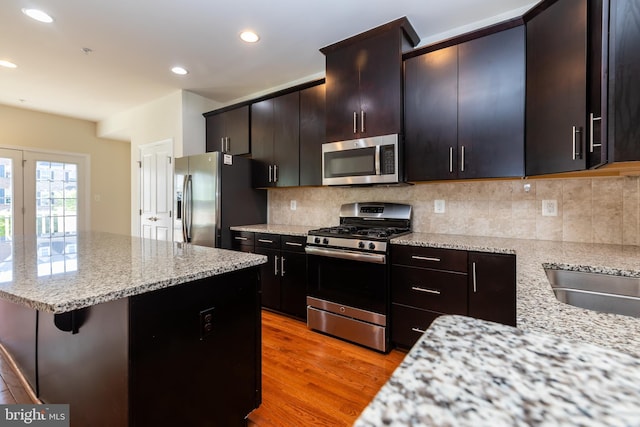 kitchen with recessed lighting, stainless steel appliances, light wood finished floors, decorative backsplash, and light stone countertops