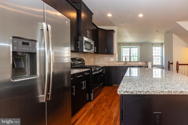 kitchen featuring light stone counters, wood finished floors, a sink, stainless steel appliances, and tasteful backsplash