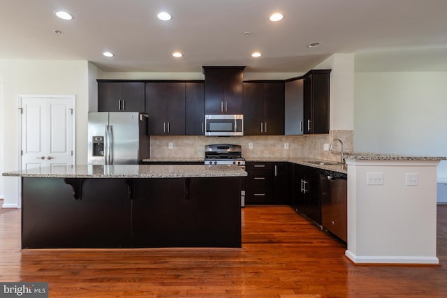 kitchen featuring a sink, a kitchen island, dark wood-style floors, stainless steel appliances, and light stone countertops