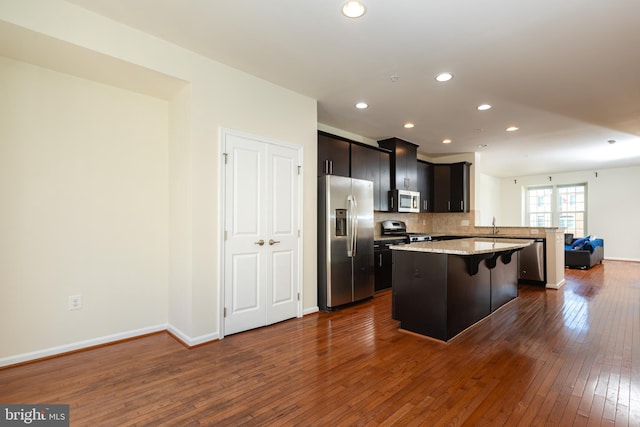 kitchen featuring a kitchen island, a breakfast bar, stainless steel appliances, dark wood-type flooring, and open floor plan