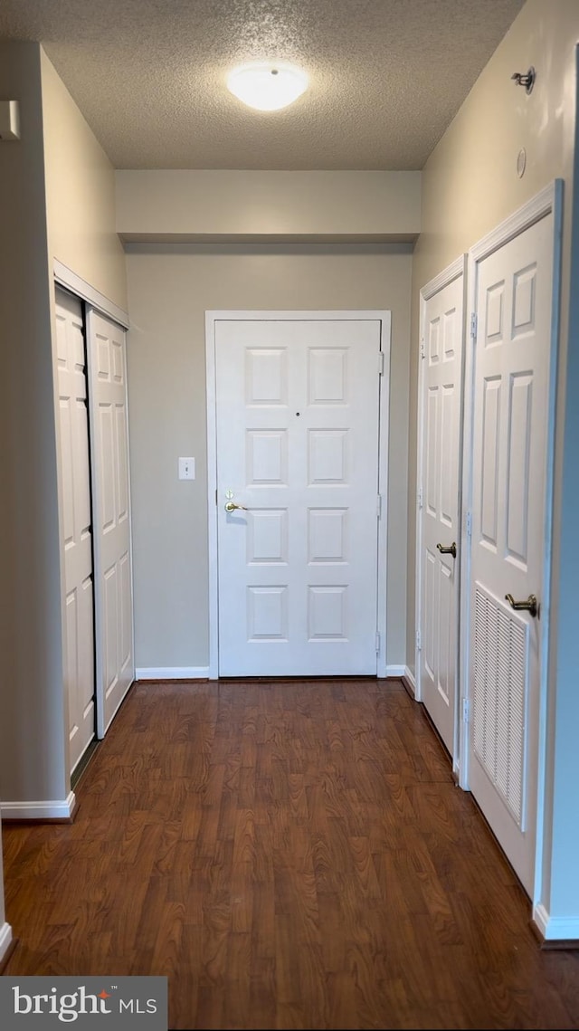 doorway to outside with a textured ceiling, dark wood-type flooring, and baseboards