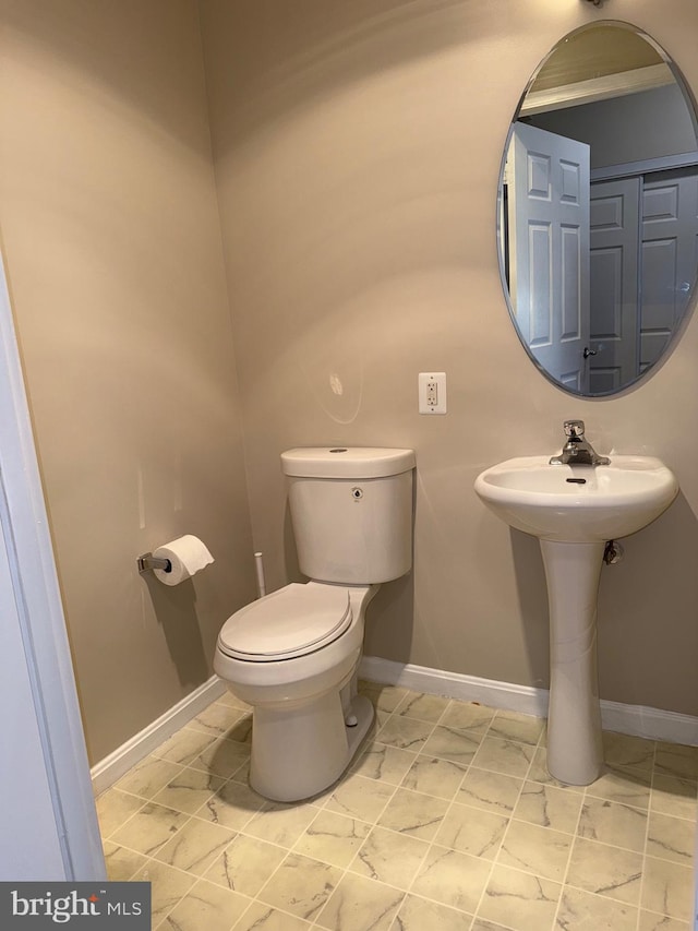 half bathroom featuring toilet, baseboards, and a sink