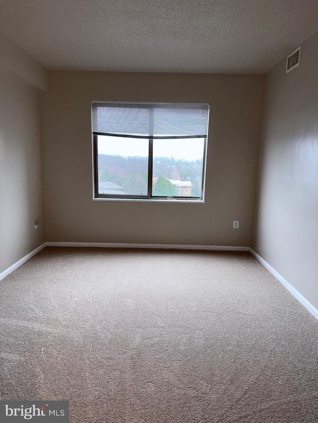 empty room with carpet, baseboards, visible vents, and a textured ceiling