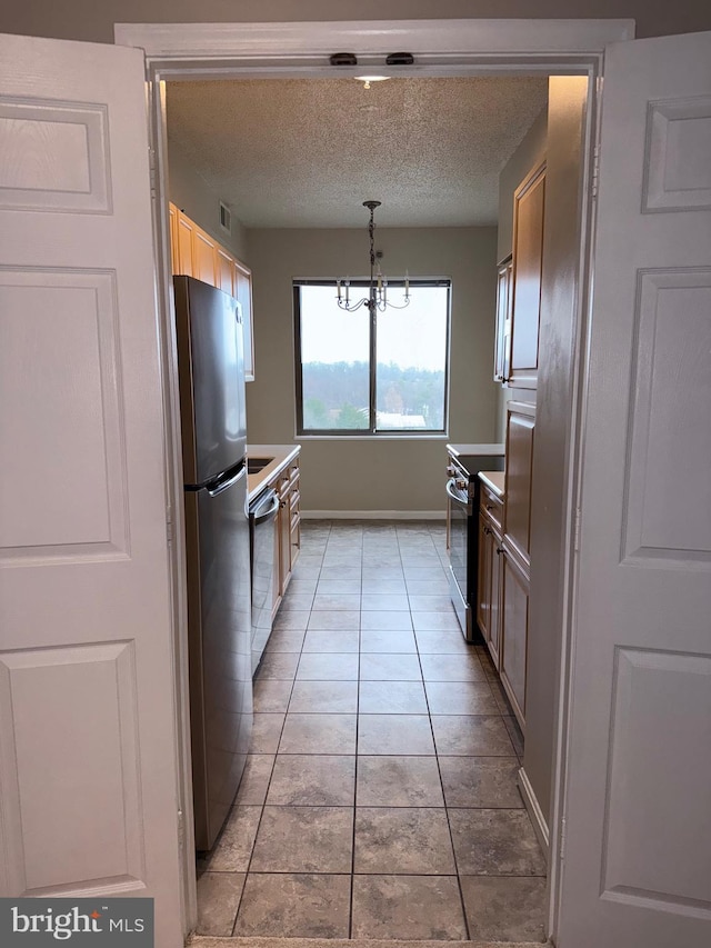 kitchen with a notable chandelier, a textured ceiling, appliances with stainless steel finishes, light tile patterned flooring, and baseboards