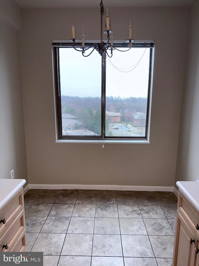 unfurnished dining area with light tile patterned floors, a notable chandelier, and baseboards