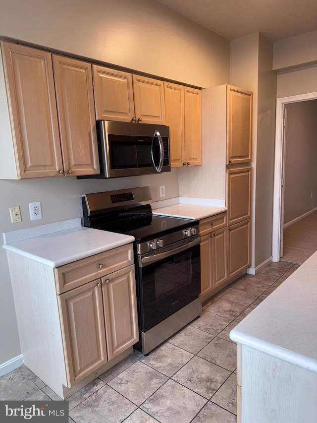 kitchen with baseboards, light brown cabinetry, light countertops, light tile patterned floors, and appliances with stainless steel finishes