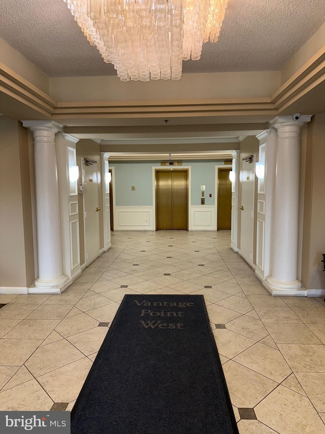 hall featuring elevator, light tile patterned floors, a decorative wall, and decorative columns