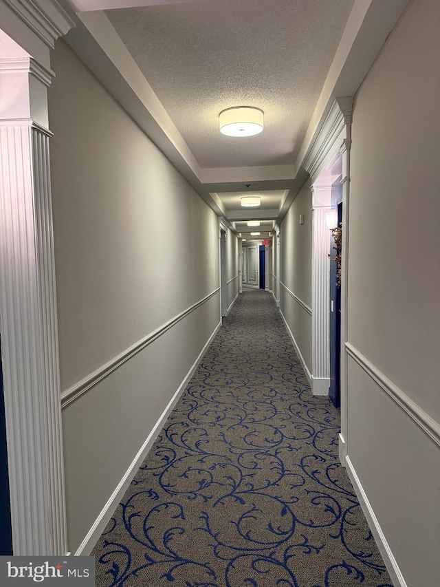 hall featuring baseboards, carpet floors, and a textured ceiling