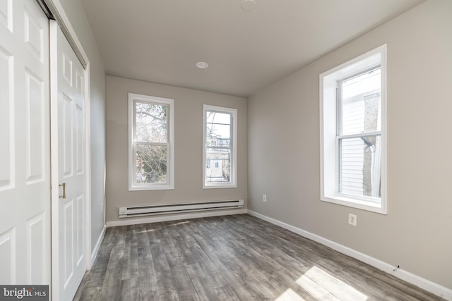 unfurnished bedroom with a baseboard heating unit, baseboards, a closet, and wood finished floors