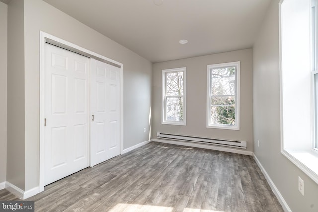 unfurnished bedroom featuring a baseboard radiator, baseboards, a closet, and wood finished floors