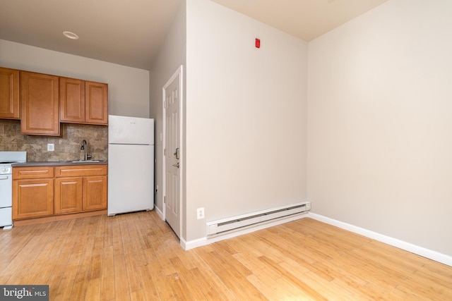 kitchen with a baseboard heating unit, dark countertops, freestanding refrigerator, light wood finished floors, and decorative backsplash