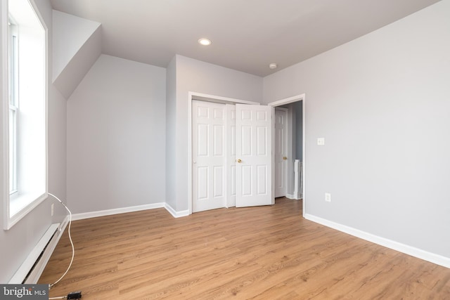 unfurnished bedroom with light wood finished floors, baseboard heating, a closet, and baseboards