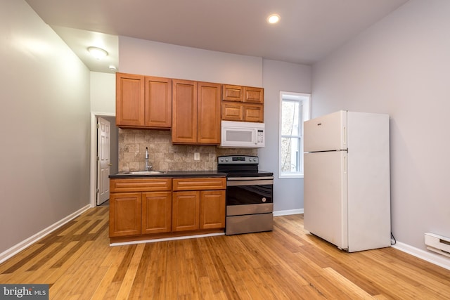 kitchen featuring dark countertops, decorative backsplash, light wood-style floors, white appliances, and a sink