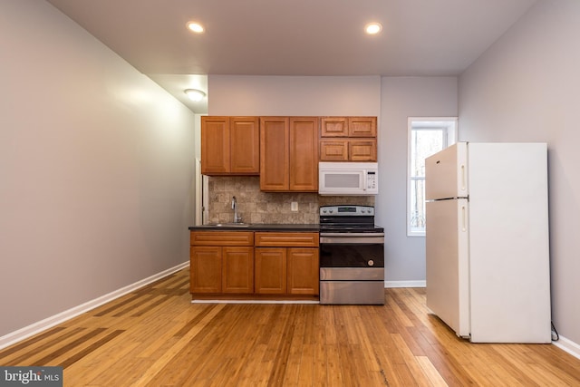 kitchen with brown cabinets, a sink, dark countertops, white appliances, and decorative backsplash