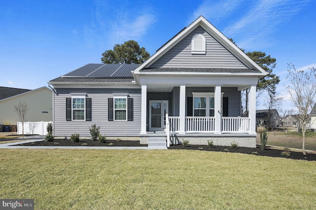 view of front facade featuring roof mounted solar panels, a porch, a front lawn, and a shingled roof