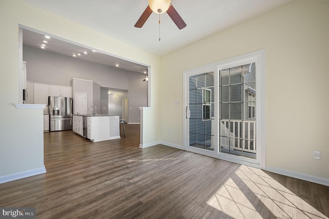 unfurnished living room with a sink, baseboards, dark wood-type flooring, and a ceiling fan