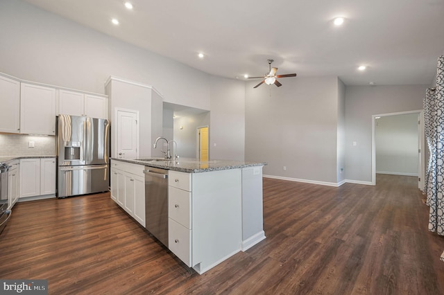 kitchen featuring a ceiling fan, dark wood finished floors, dark stone counters, a sink, and appliances with stainless steel finishes