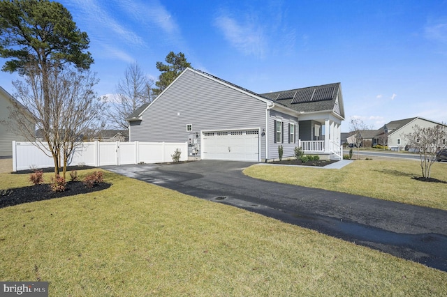 view of side of home with fence, driveway, a yard, a garage, and roof mounted solar panels