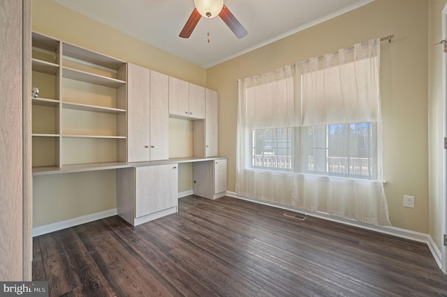 unfurnished office with a ceiling fan, visible vents, baseboards, built in study area, and dark wood finished floors