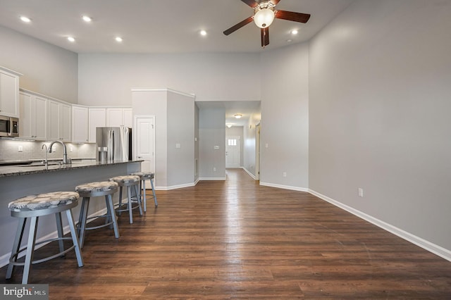 kitchen with ceiling fan, dark wood finished floors, a breakfast bar, appliances with stainless steel finishes, and white cabinetry