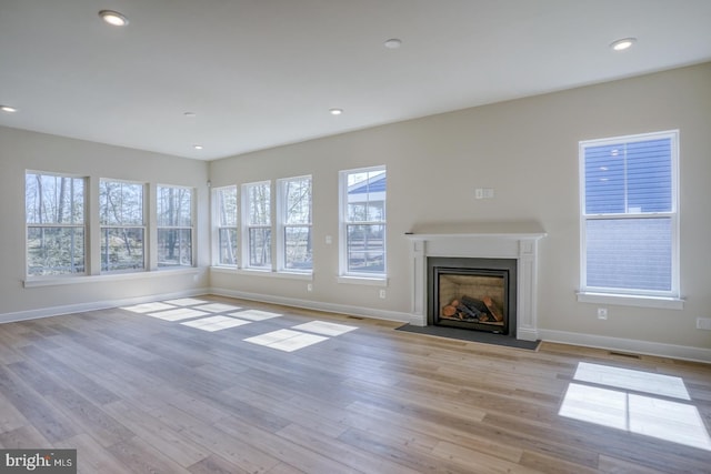 unfurnished living room with recessed lighting, a fireplace with flush hearth, light wood-style flooring, and baseboards