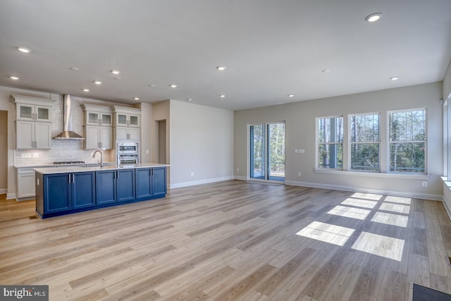 kitchen with stainless steel appliances, light countertops, white cabinetry, wall chimney range hood, and light wood-type flooring