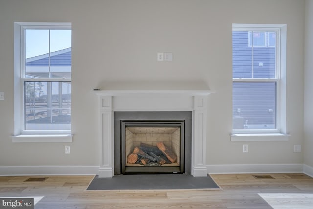 interior details with a fireplace with flush hearth, wood finished floors, visible vents, and baseboards