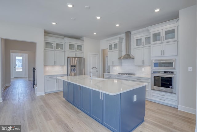 kitchen featuring blue cabinets, a sink, appliances with stainless steel finishes, wall chimney exhaust hood, and a large island with sink