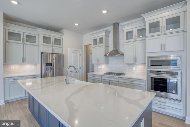 kitchen with light wood finished floors, a spacious island, a sink, stainless steel appliances, and wall chimney exhaust hood