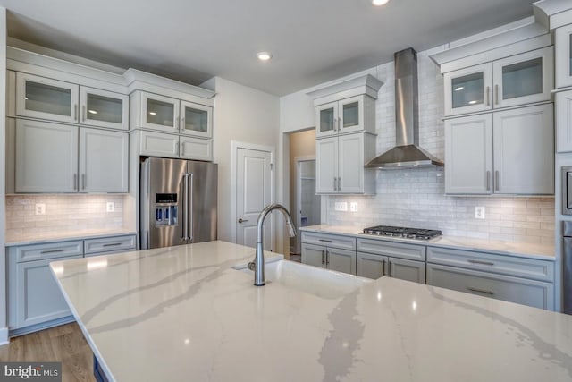 kitchen with wood finished floors, a sink, stainless steel appliances, wall chimney range hood, and tasteful backsplash