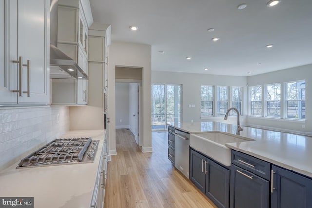 kitchen featuring a sink, white cabinets, appliances with stainless steel finishes, wall chimney exhaust hood, and a wealth of natural light