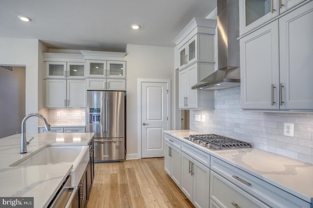 kitchen with light wood finished floors, wall chimney range hood, recessed lighting, appliances with stainless steel finishes, and white cabinetry