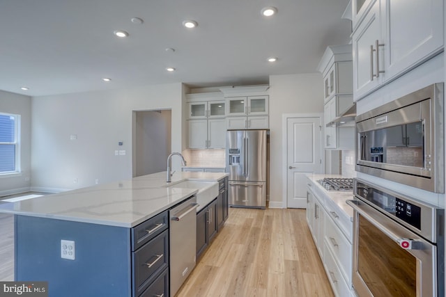 kitchen with light wood-type flooring, a kitchen island with sink, a sink, white cabinetry, and stainless steel appliances