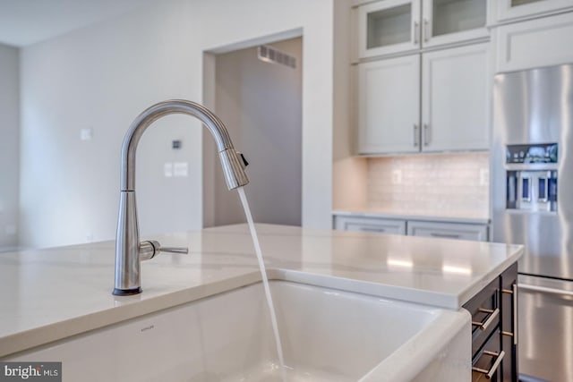 details with visible vents, backsplash, stainless steel refrigerator with ice dispenser, white cabinetry, and a sink