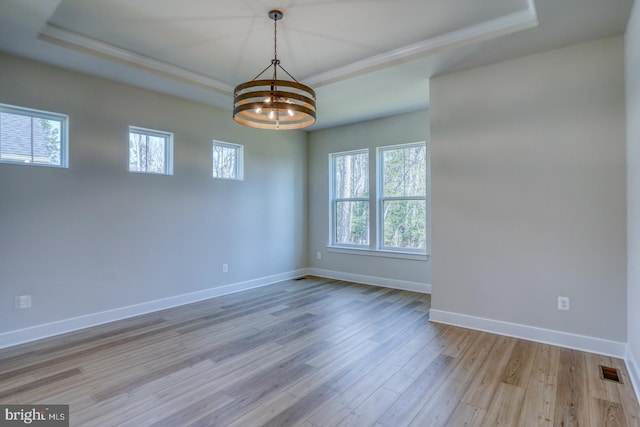 unfurnished room featuring a raised ceiling, an inviting chandelier, and wood finished floors