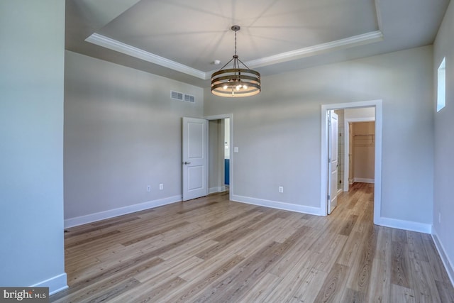 empty room featuring light wood-type flooring, visible vents, a raised ceiling, an inviting chandelier, and baseboards