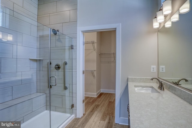 bathroom with a walk in closet, a stall shower, wood finished floors, baseboards, and vanity