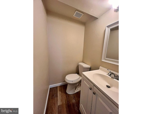 half bath with visible vents, toilet, wood finished floors, baseboards, and vanity