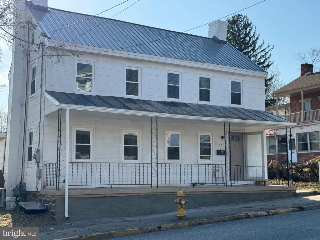 view of front of house with metal roof, a porch, a chimney, and a standing seam roof