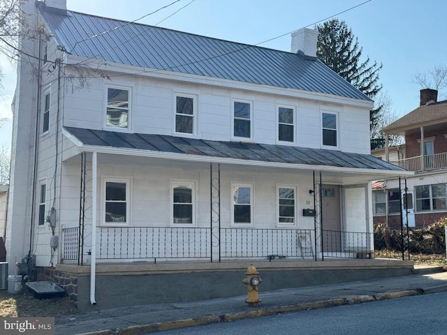 view of front of house with metal roof, a porch, a chimney, and a standing seam roof