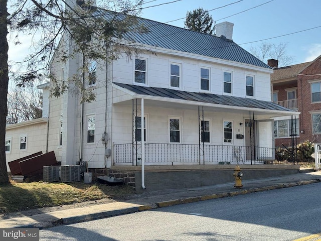 view of front of property featuring a standing seam roof, covered porch, central AC, a chimney, and metal roof