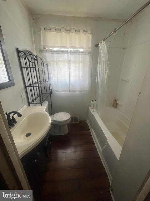 full bathroom featuring a wealth of natural light, shower / bathtub combination with curtain, toilet, wood finished floors, and vanity