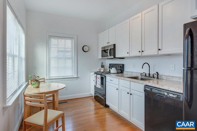 kitchen with a sink, light wood-type flooring, black appliances, and white cabinets