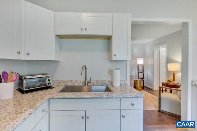 kitchen with a sink, light stone counters, wood finished floors, white cabinets, and a toaster