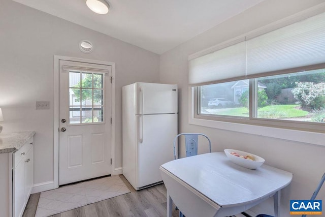 kitchen featuring baseboards, vaulted ceiling, freestanding refrigerator, light wood-style floors, and white cabinets