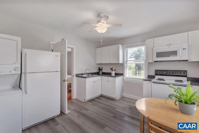 kitchen featuring light wood-type flooring, stacked washer and clothes dryer, white appliances, white cabinetry, and a ceiling fan