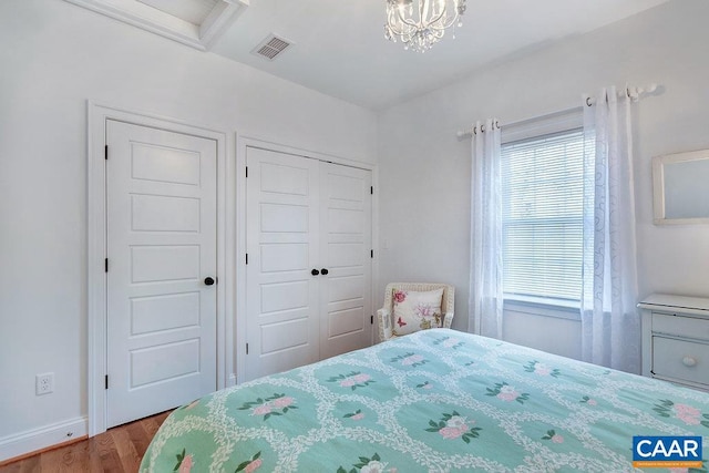 bedroom with visible vents, wood finished floors, a closet, an inviting chandelier, and baseboards