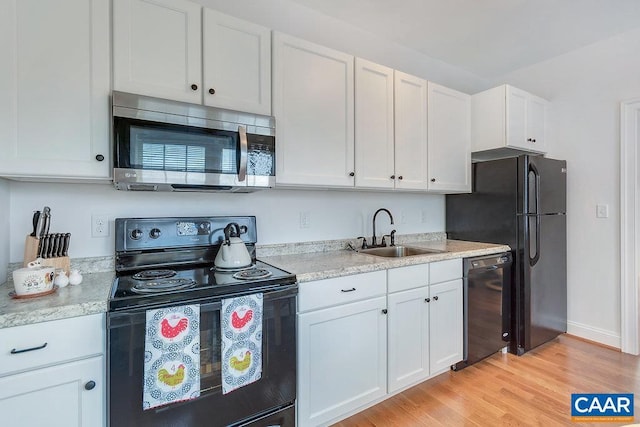 kitchen with baseboards, light wood-style flooring, white cabinets, black appliances, and a sink