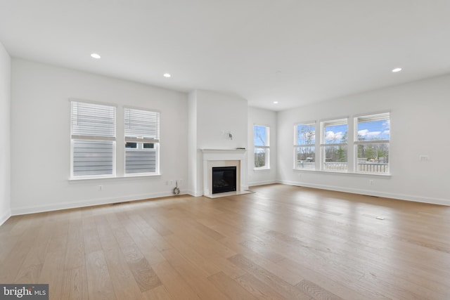 unfurnished living room featuring recessed lighting, a healthy amount of sunlight, a fireplace with flush hearth, and light wood-style floors