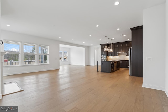 unfurnished living room with a sink, baseboards, light wood-style floors, and recessed lighting